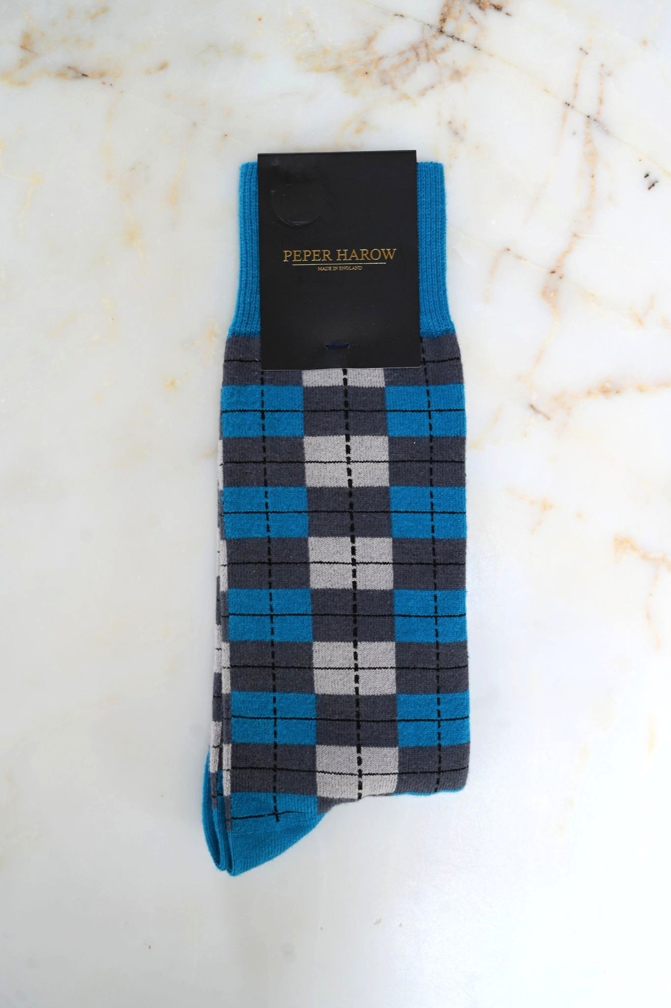 Blue and gray checkered sock with Peter Harrow packaging on a marble background