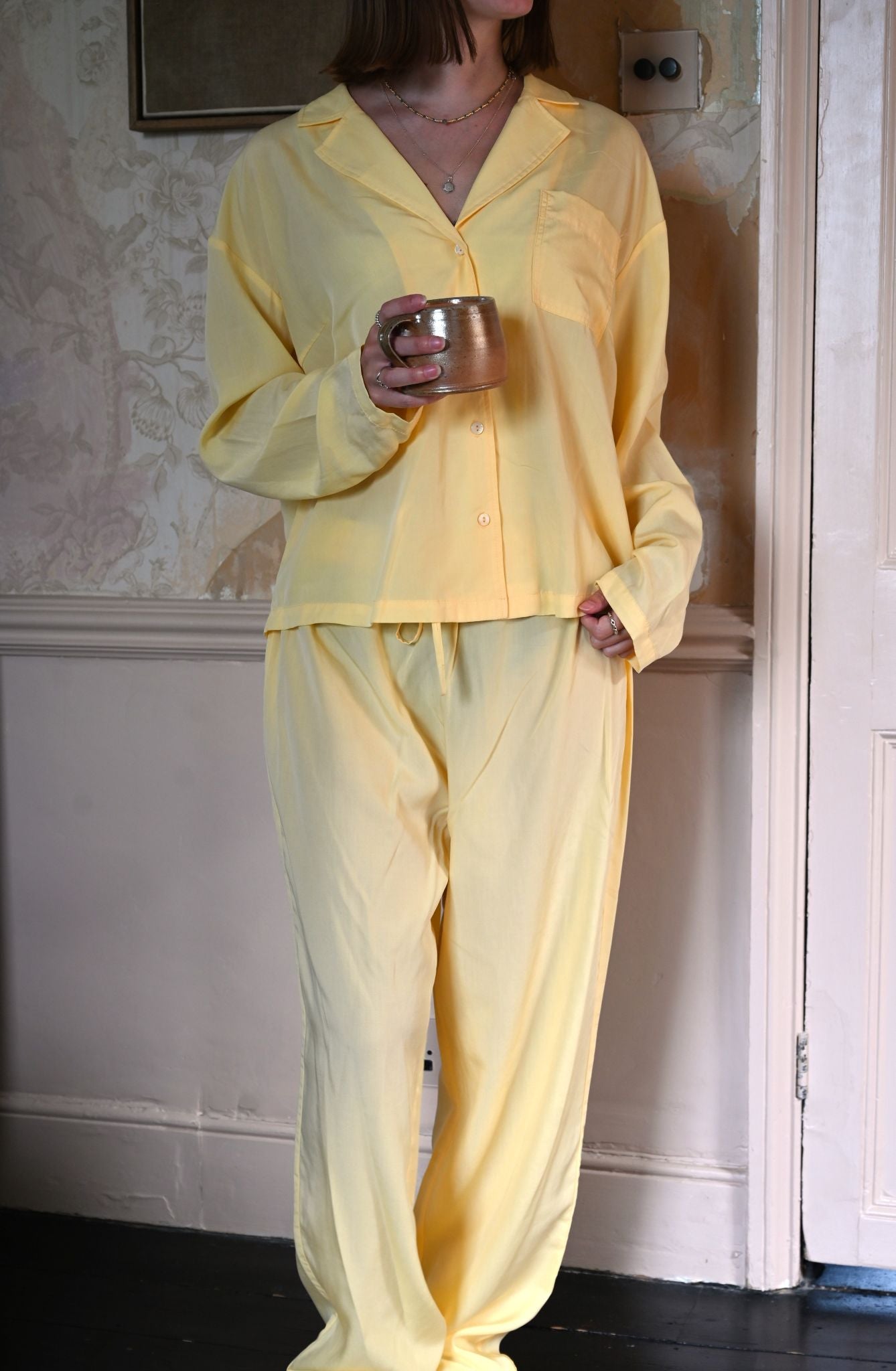 Person wearing yellow pajamas holding a cup in a room with floral wallpaper.