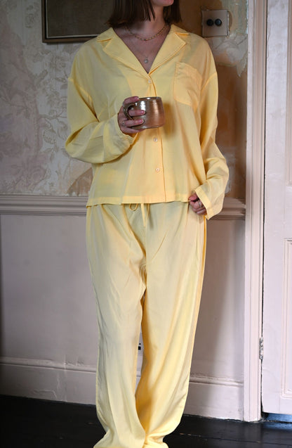 Person wearing yellow pajamas holding a cup in a room with floral wallpaper.
