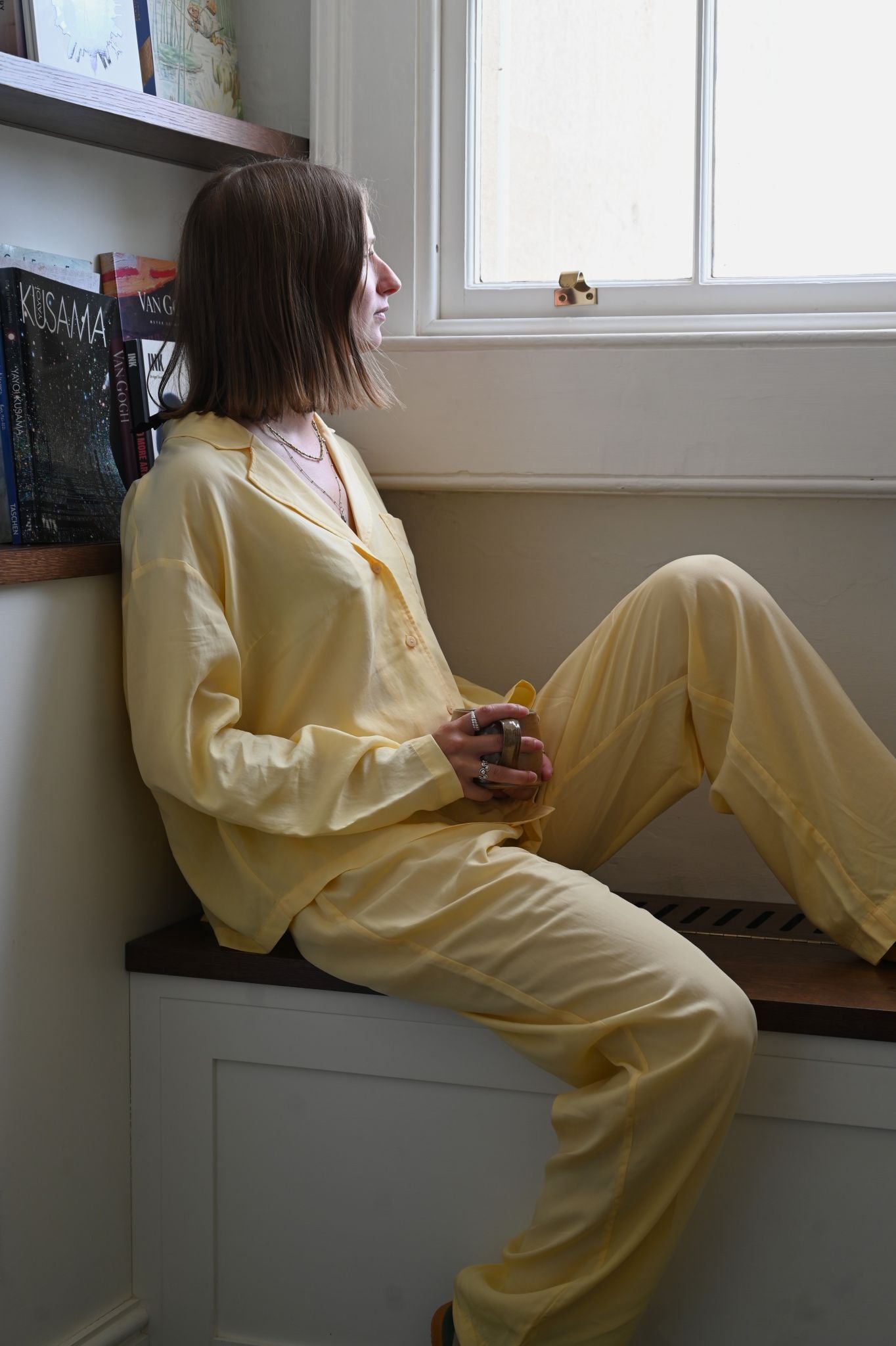 Person wearing yellow pajamas sitting on a windowsill.