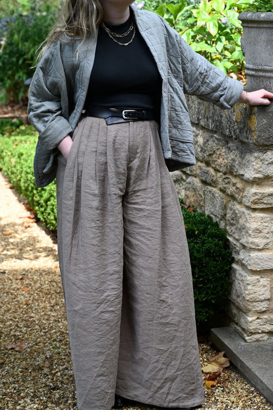 Sage grey quilted jacket with geometric stitching and large front pockets in a garden setting.
