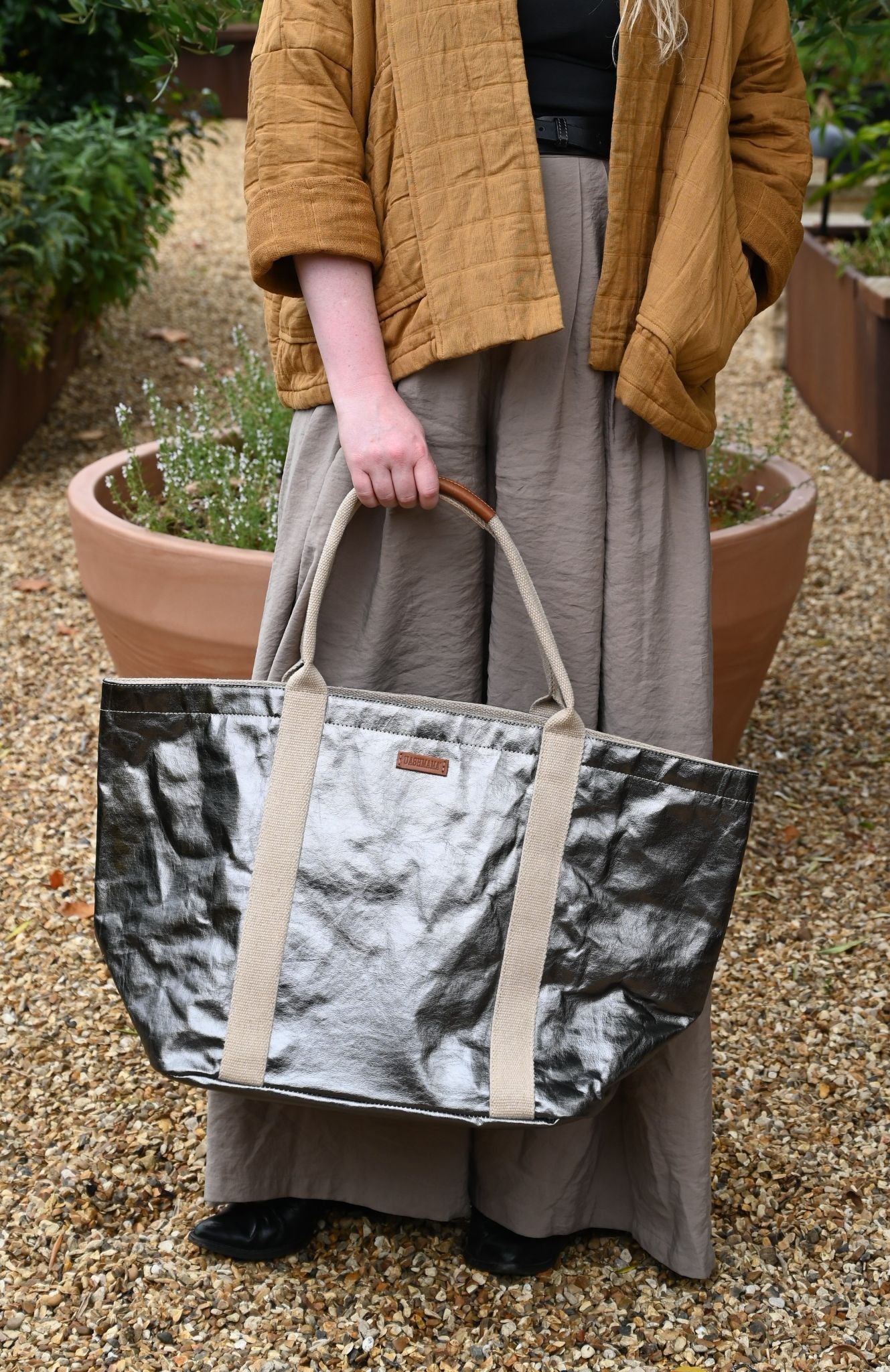 Person holding a large tote bag with a textured pattern outdoors.