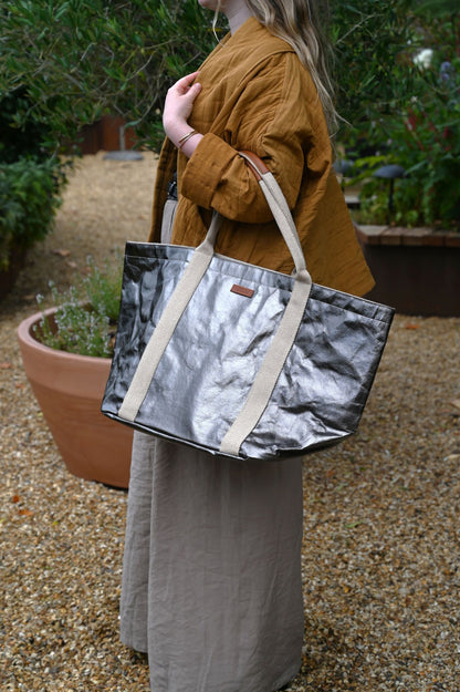 Person holding a silver and beige tote bag outdoors