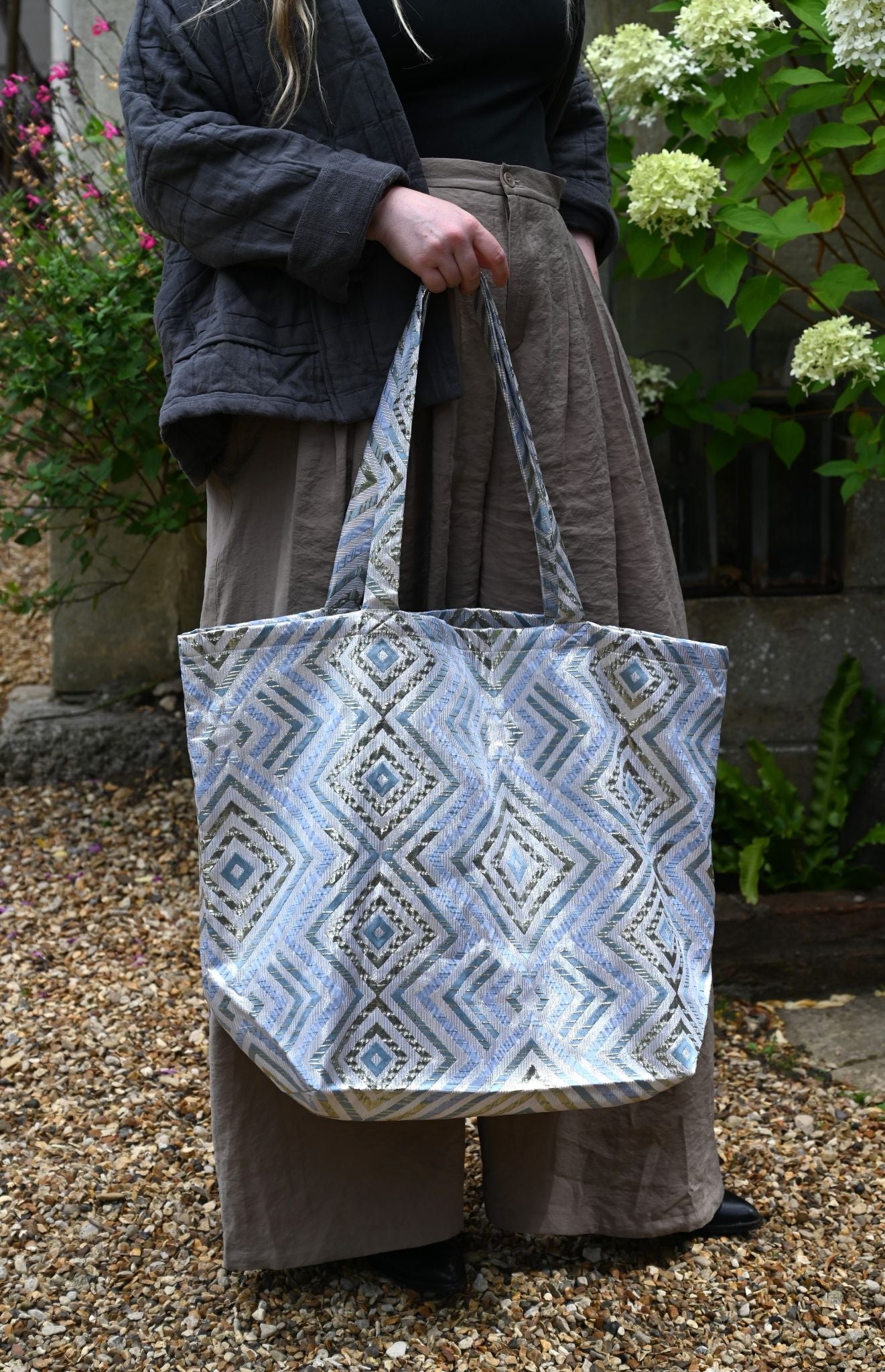 Person holding a patterned tote bag outdoors with greenery in the background