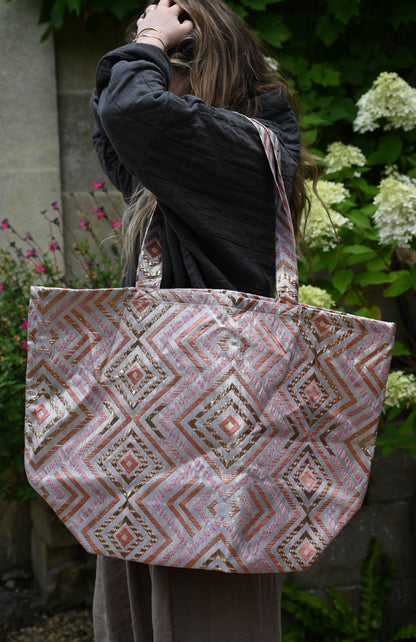 Person holding a patterned tote bag outdoors with greenery and flowers in the background