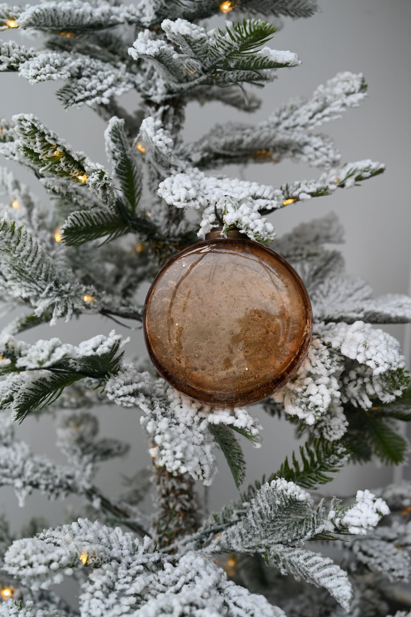 Textured amber hand-blown glass circular bauble hanging on a flocked Christmas tree.
