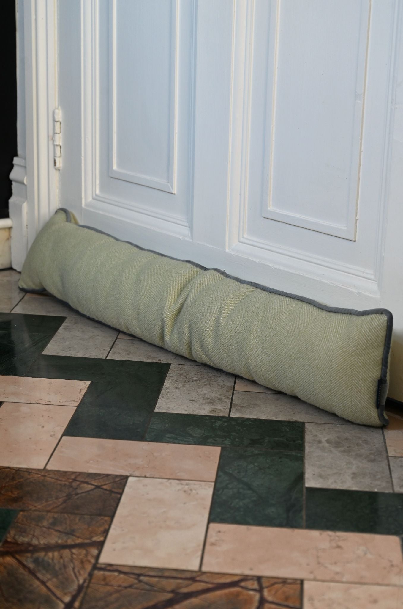 Green door stopper on a tiled floor in front of a white door.