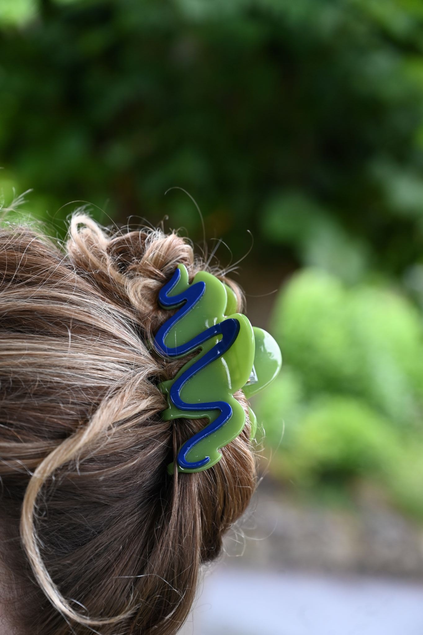 Close-up of a hair tie with a wavy design in green and blue on blurred green foliage background