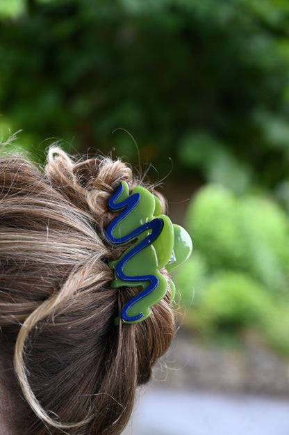 Close-up of a hair tie with a wavy design in green and blue on blurred green foliage background