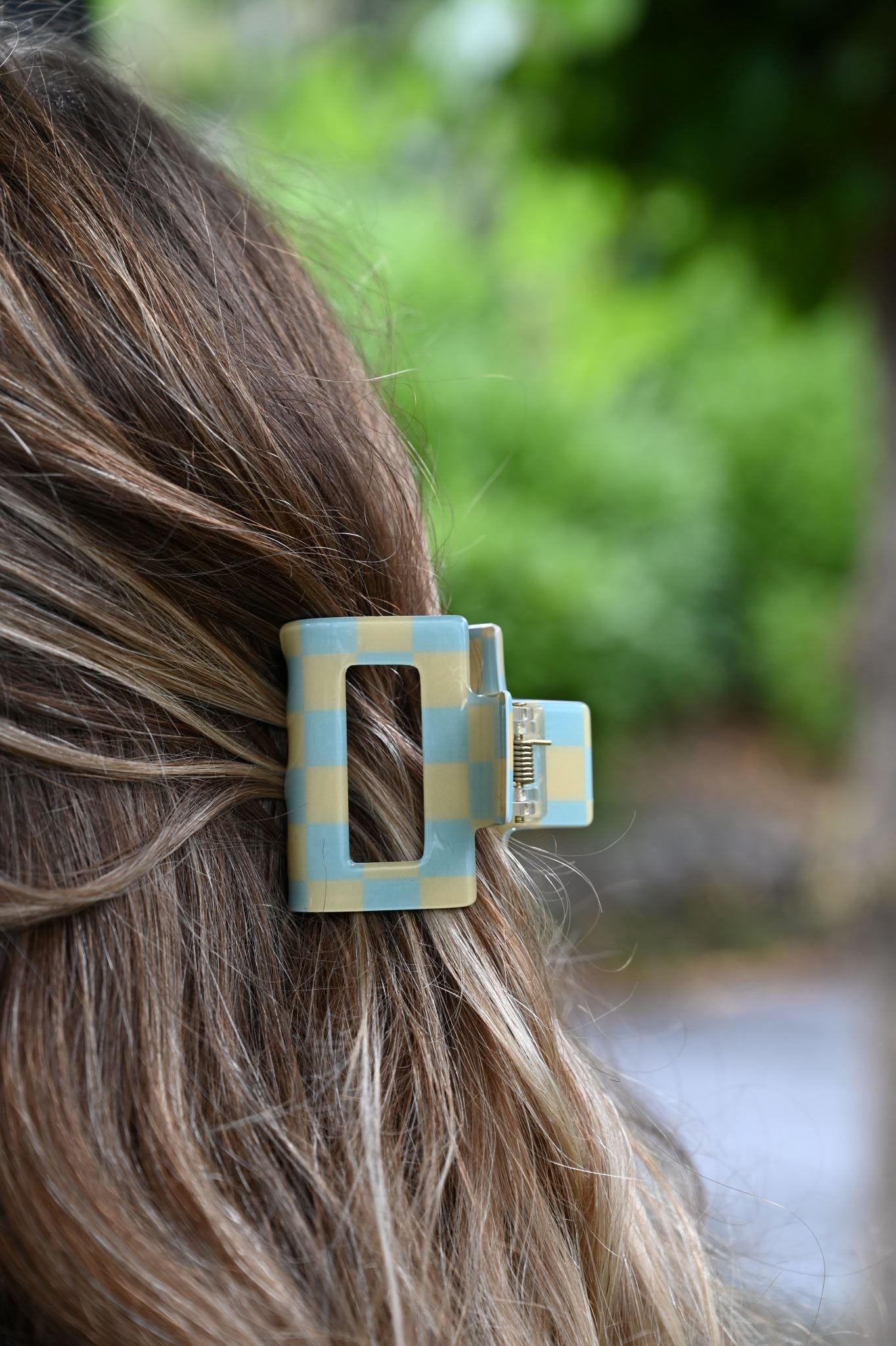 Close-up of a checkered hair clip in a person's hair with a blurred green background