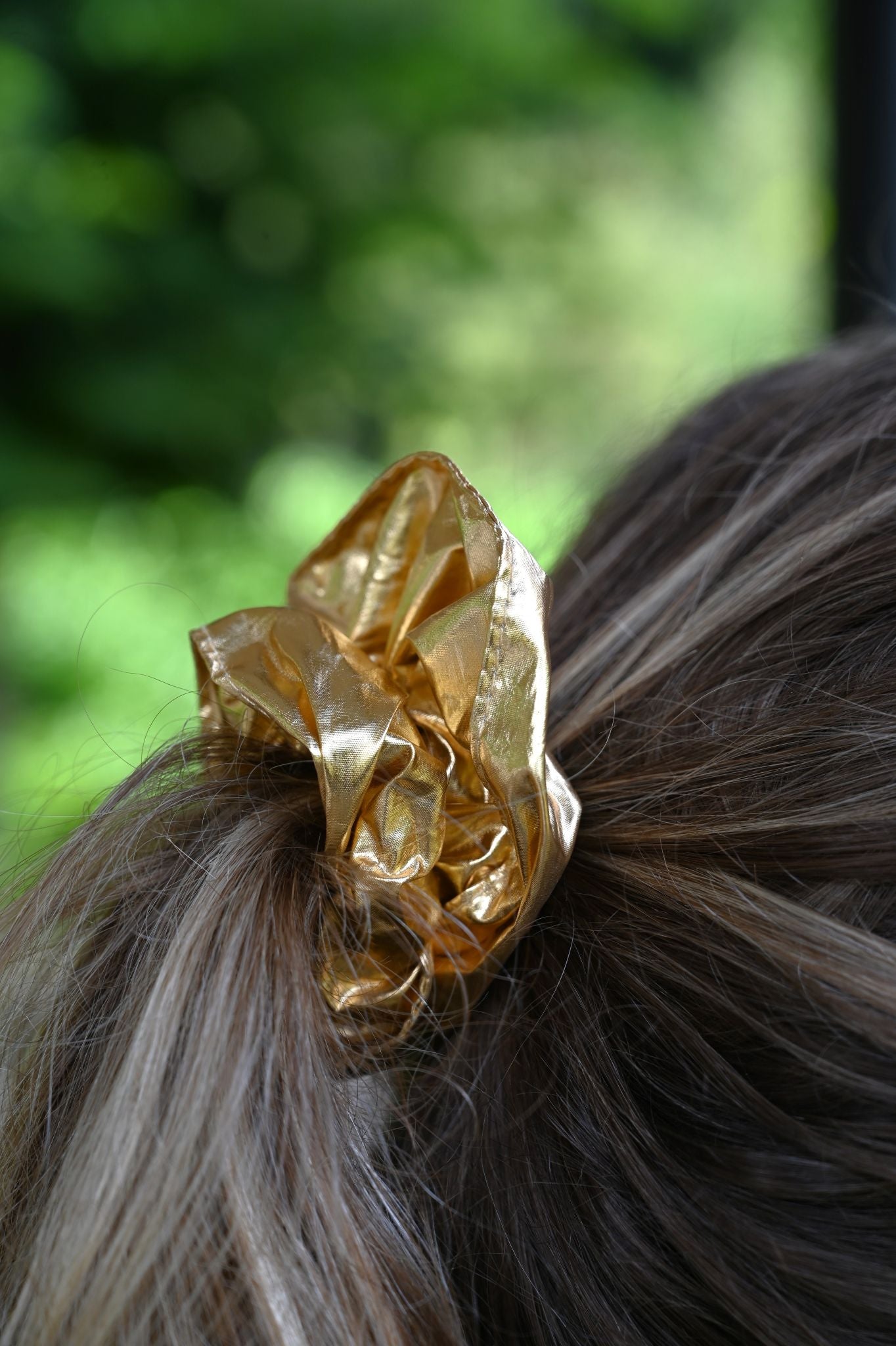 Gold scrunchie on a person's hair with a blurred green background