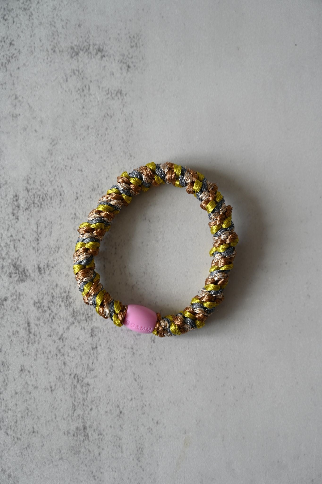 Colorful beaded hair tie with a pink bead on a gray surface