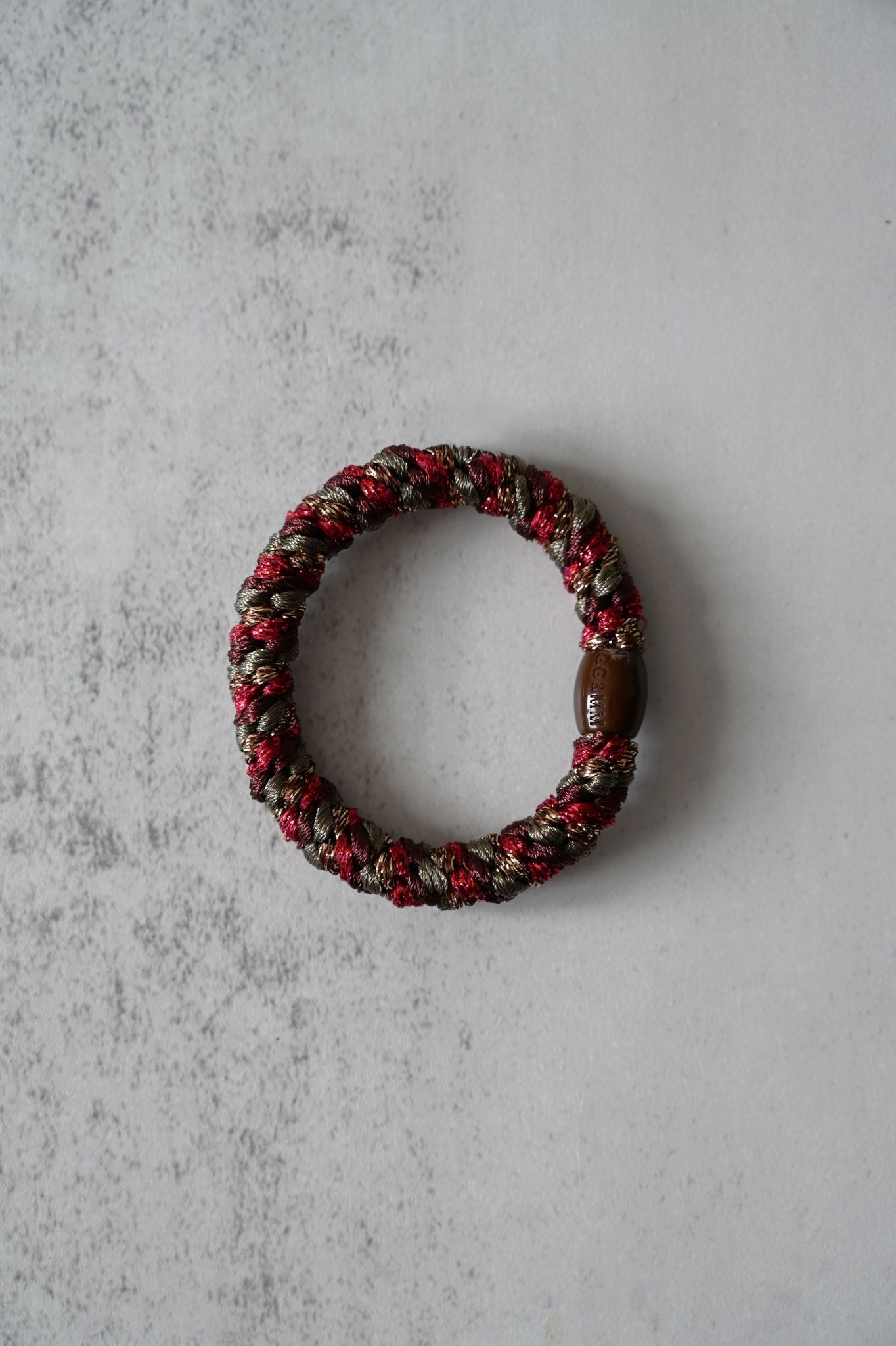 Hair tie with red and brown beads on a textured gray surface