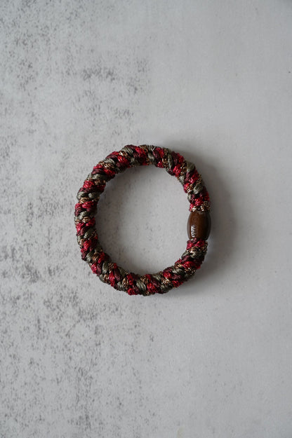 Hair tie with red and brown beads on a textured gray surface