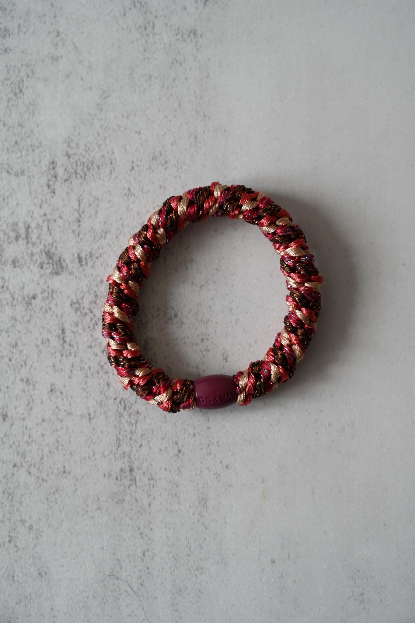 Hair tie with braided design and purple accents on a gray surface