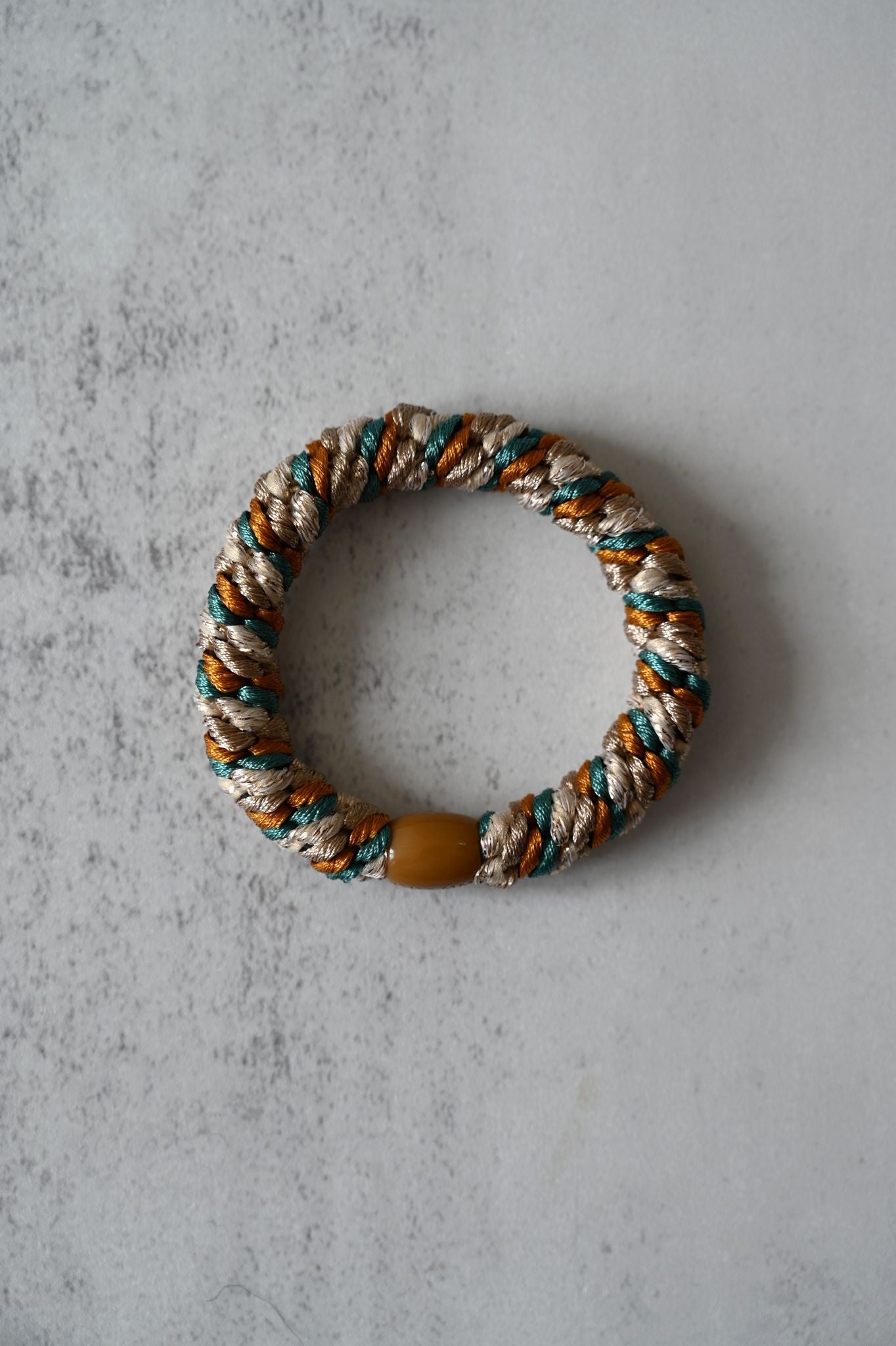Rope hair tie with a yellow bead on a textured gray background
