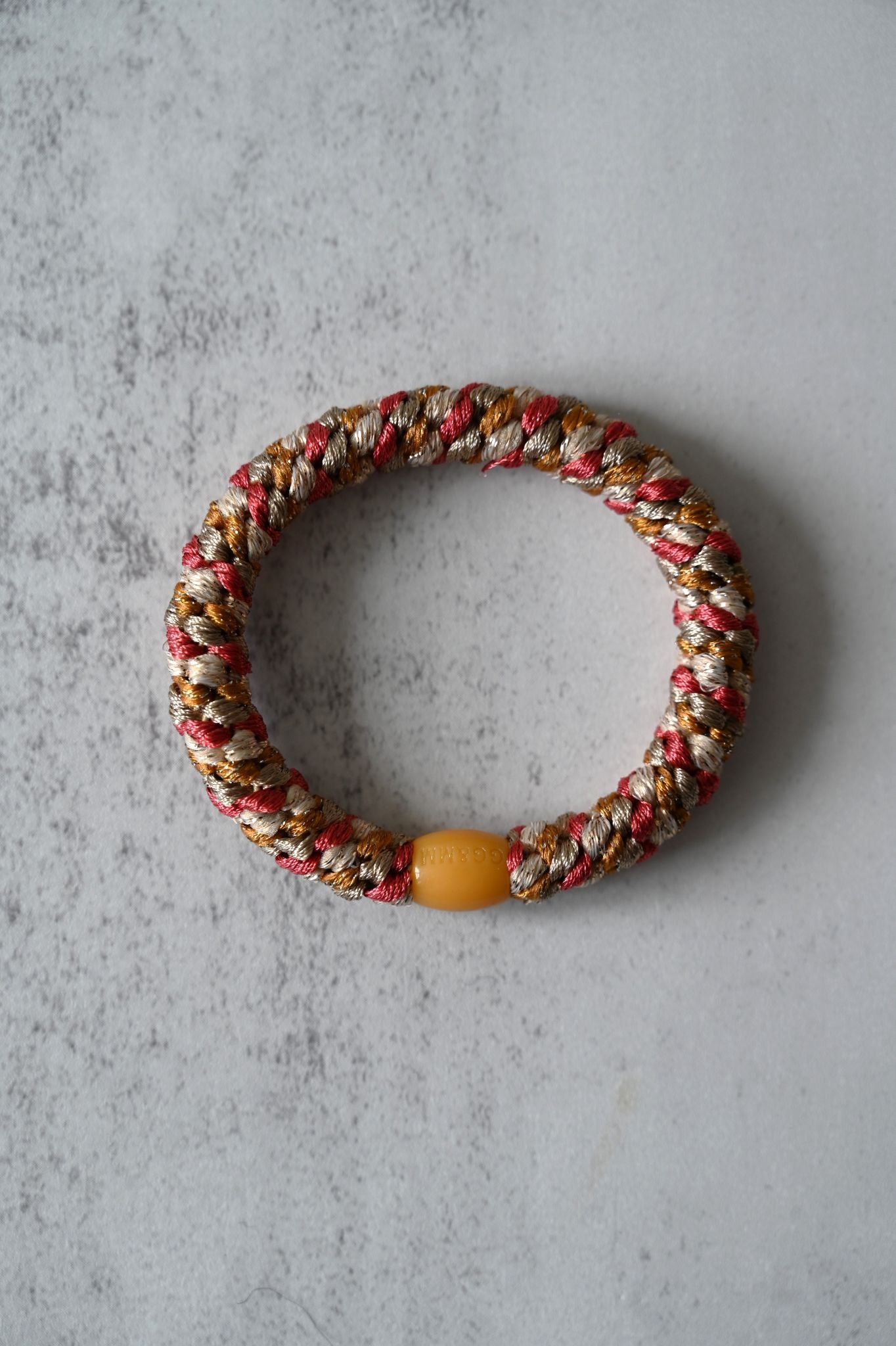 Multicolored braided hair tie with a yellow bead on a gray surface