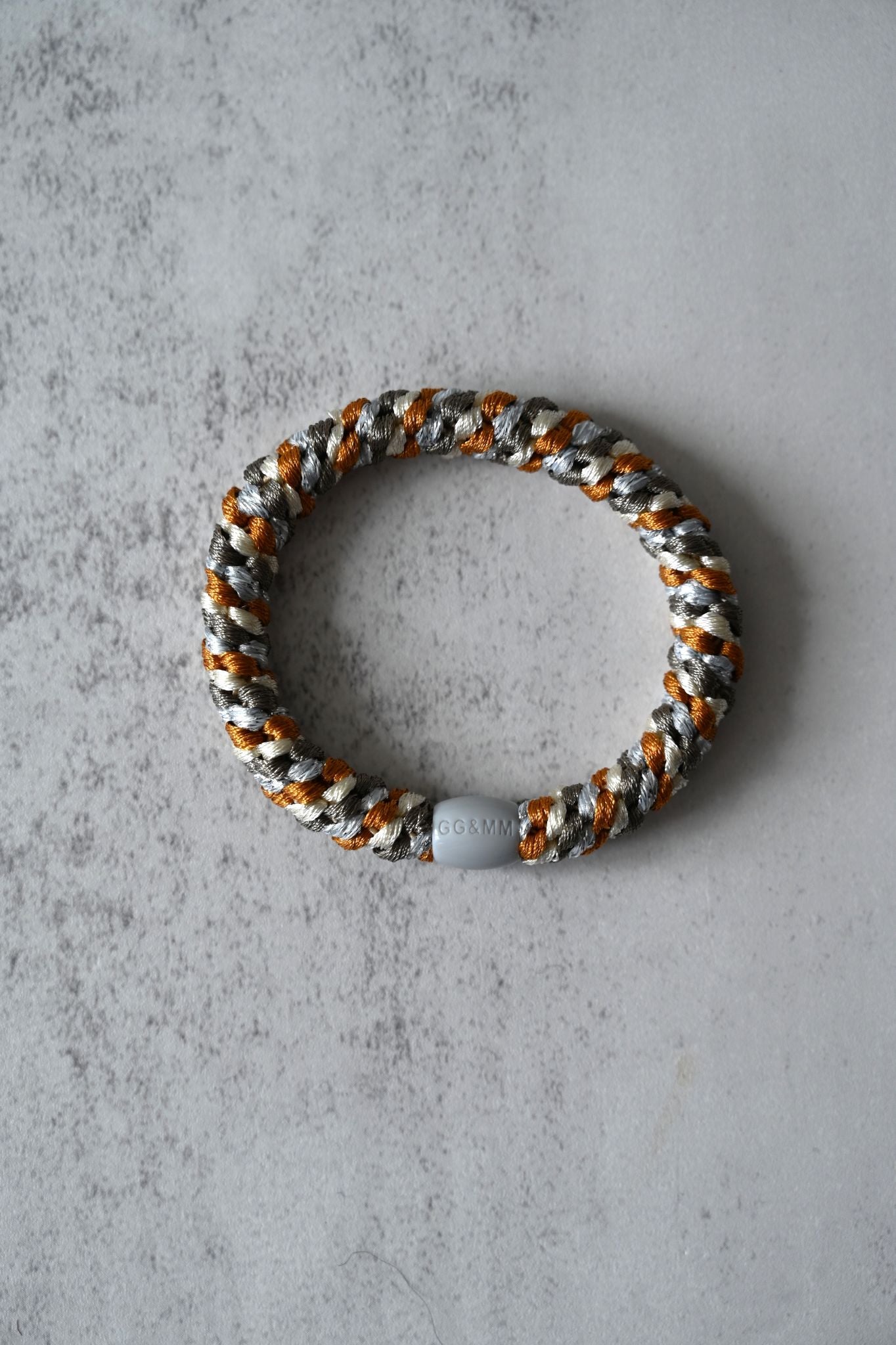 Hair tie with gray, orange, and white pattern on a gray concrete surface