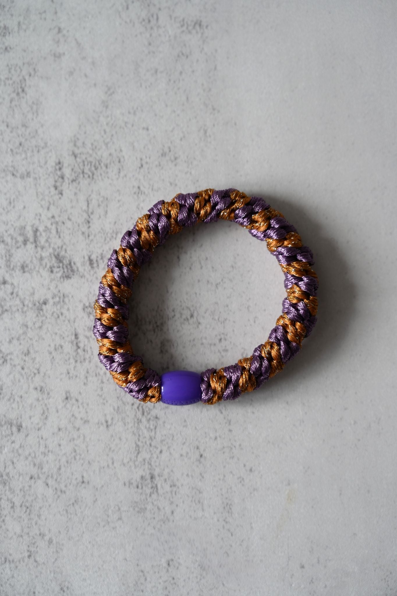 Hair tie with purple and gold pattern on a gray surface