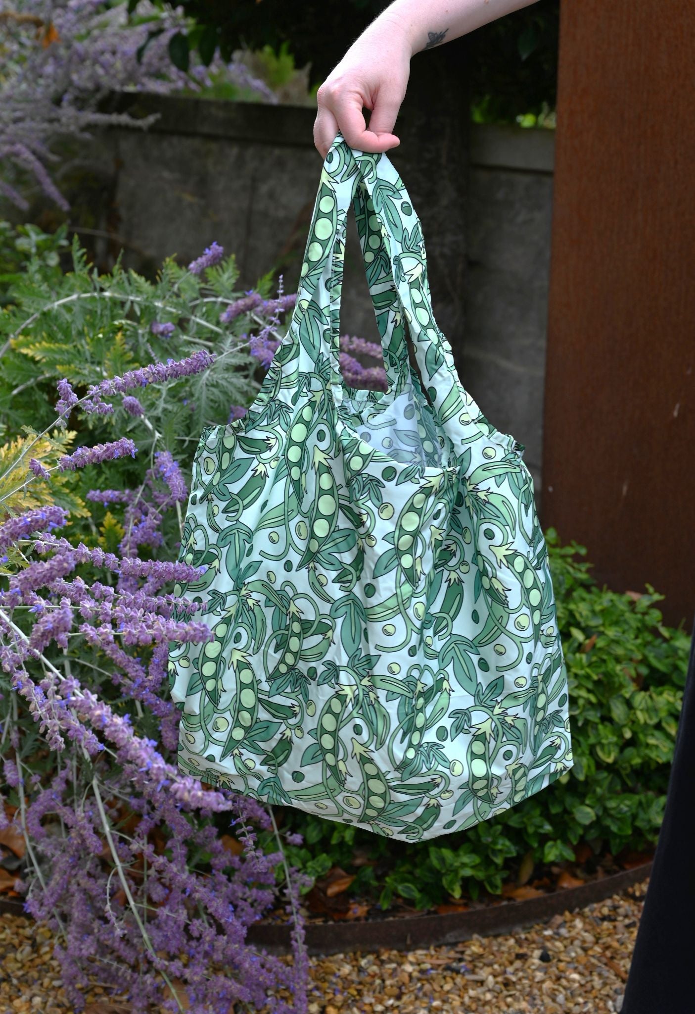Mint green reusable tote bag with a botanical pea pod print held in a garden.