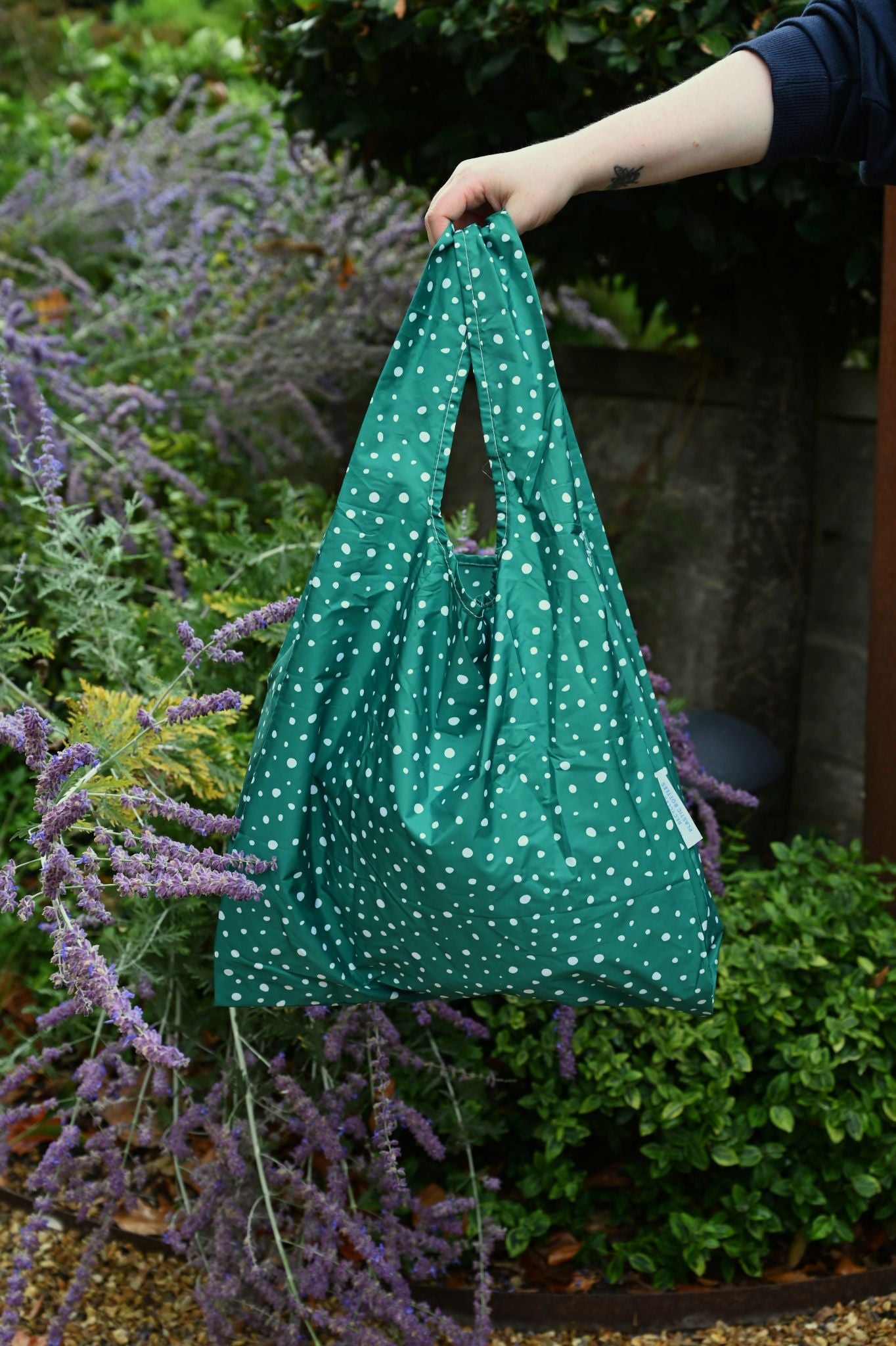 Mint green reusable tote bag with a botanical pea pod print held in a garden.