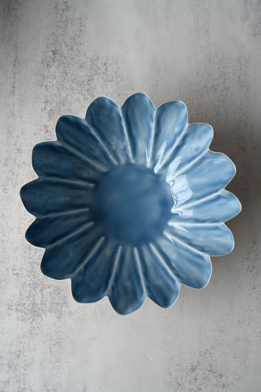 Scalloped metal bowl with a blue interior and peach exterior filled with fresh lemons.