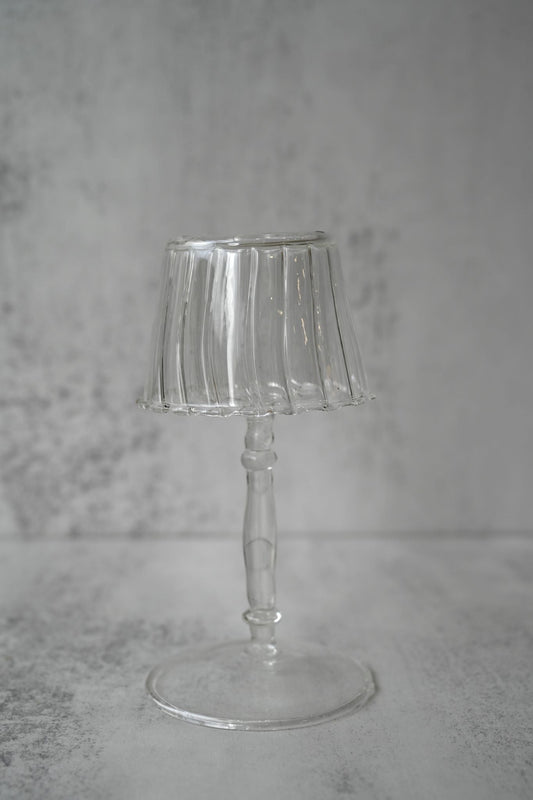 Stemmed fluted clear glass tea light holder on a silver tray in a cozy setting.