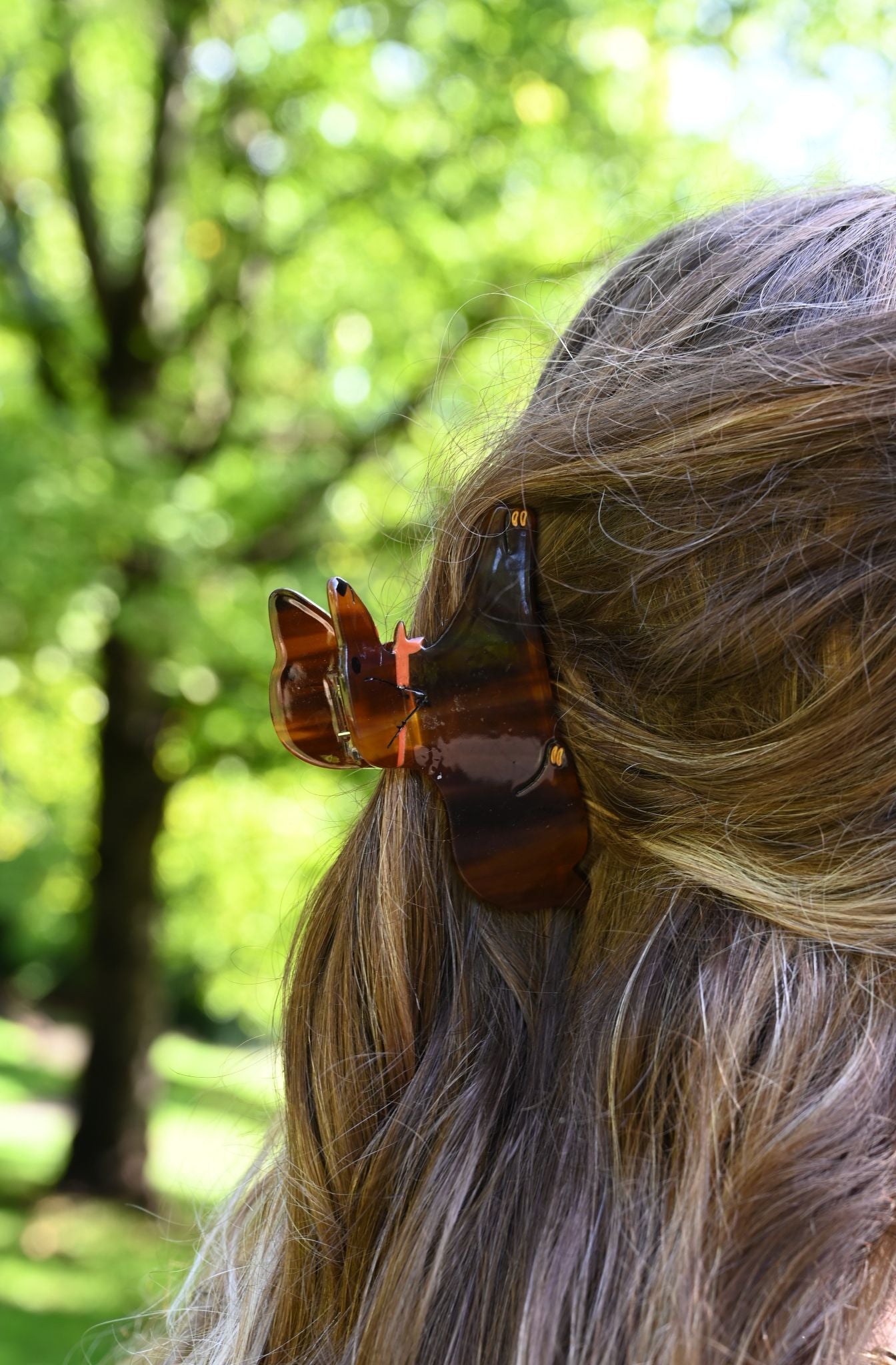 Close-up of a person's hair with a large sausage dog hair claw against a blurred green outdoor background