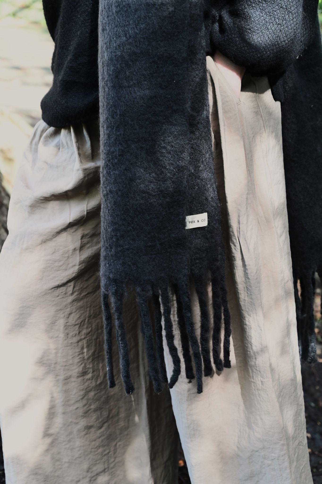 Person wearing a black scarf with fringes, standing outdoors.