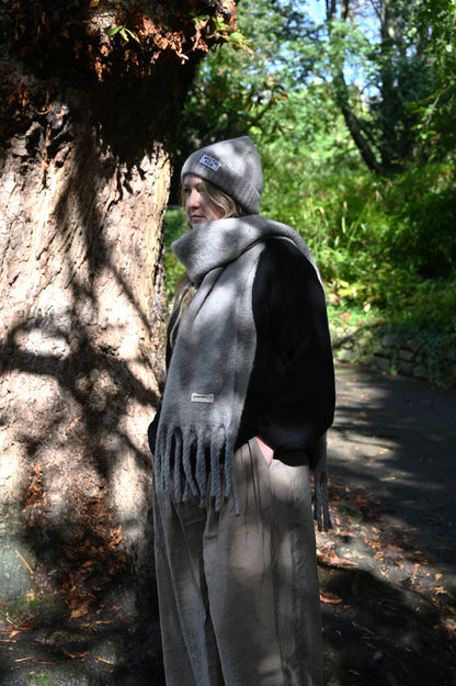 Person wearing a gray scarf and hat standing next to a tree in a forest