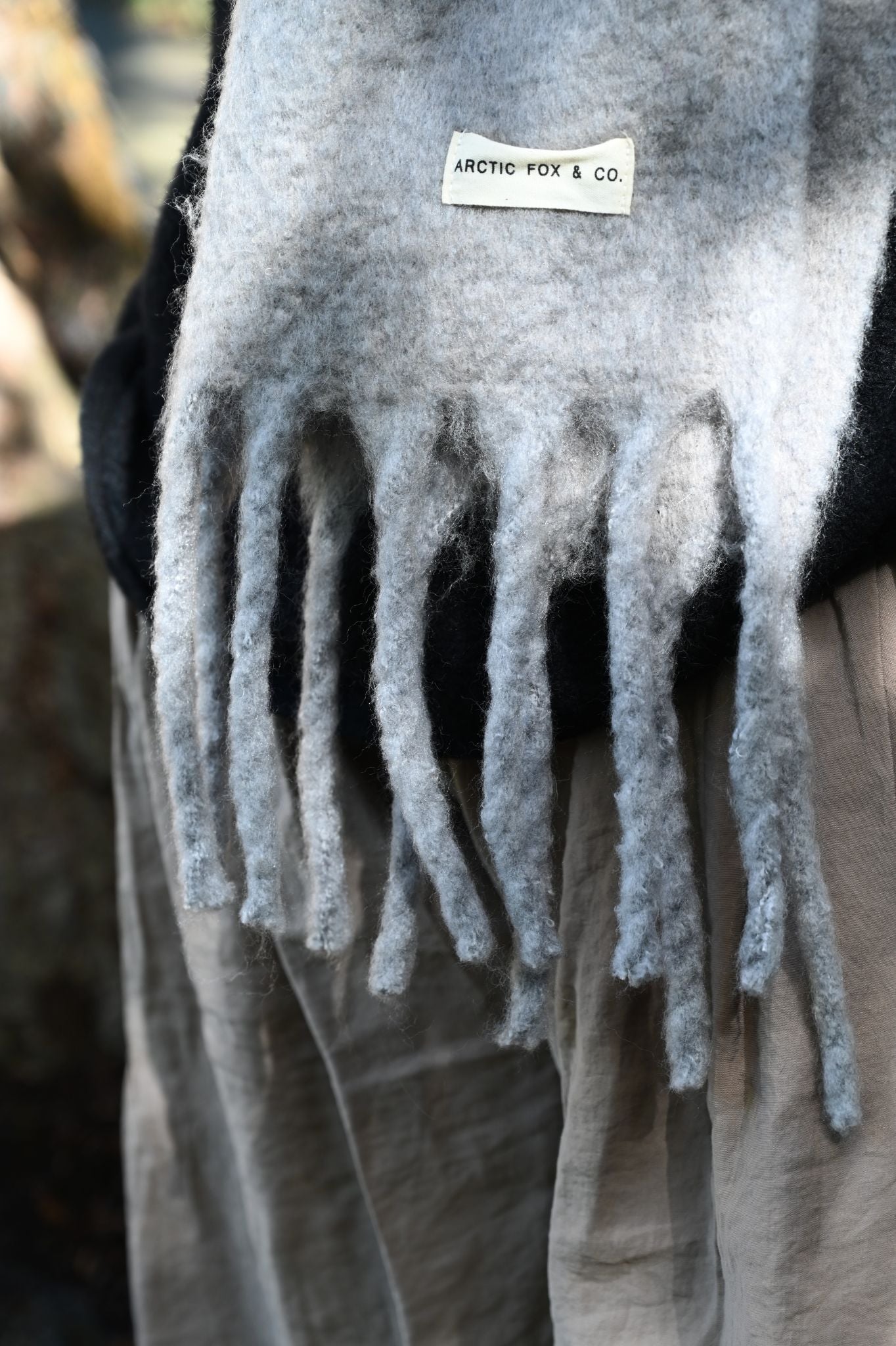 Gray scarf with fringes and a brand label on a blurred background