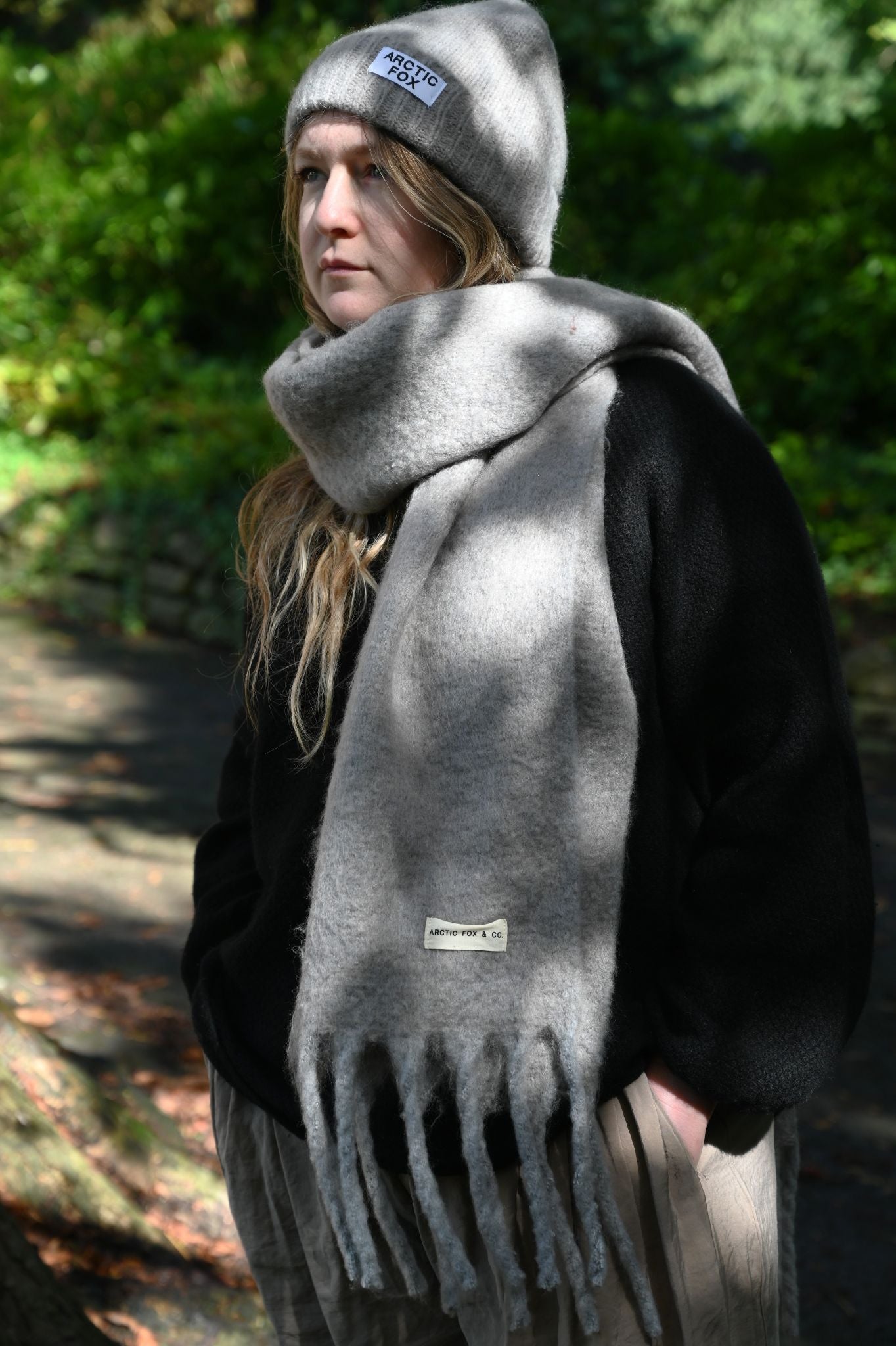 Person wearing a gray scarf and beanie with visible branding in an outdoor setting.