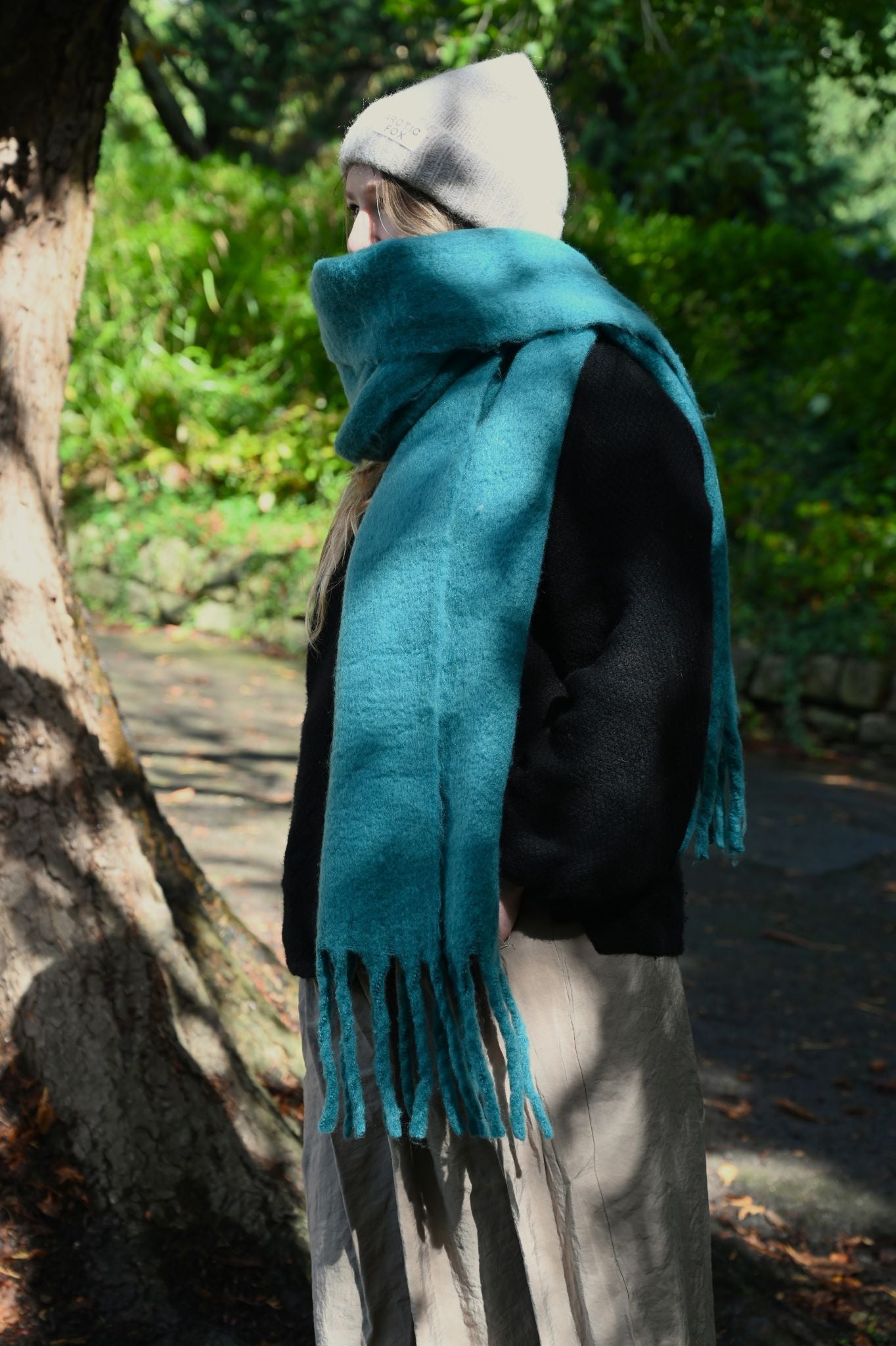 Person wearing a teal scarf and gray beanie in a park setting