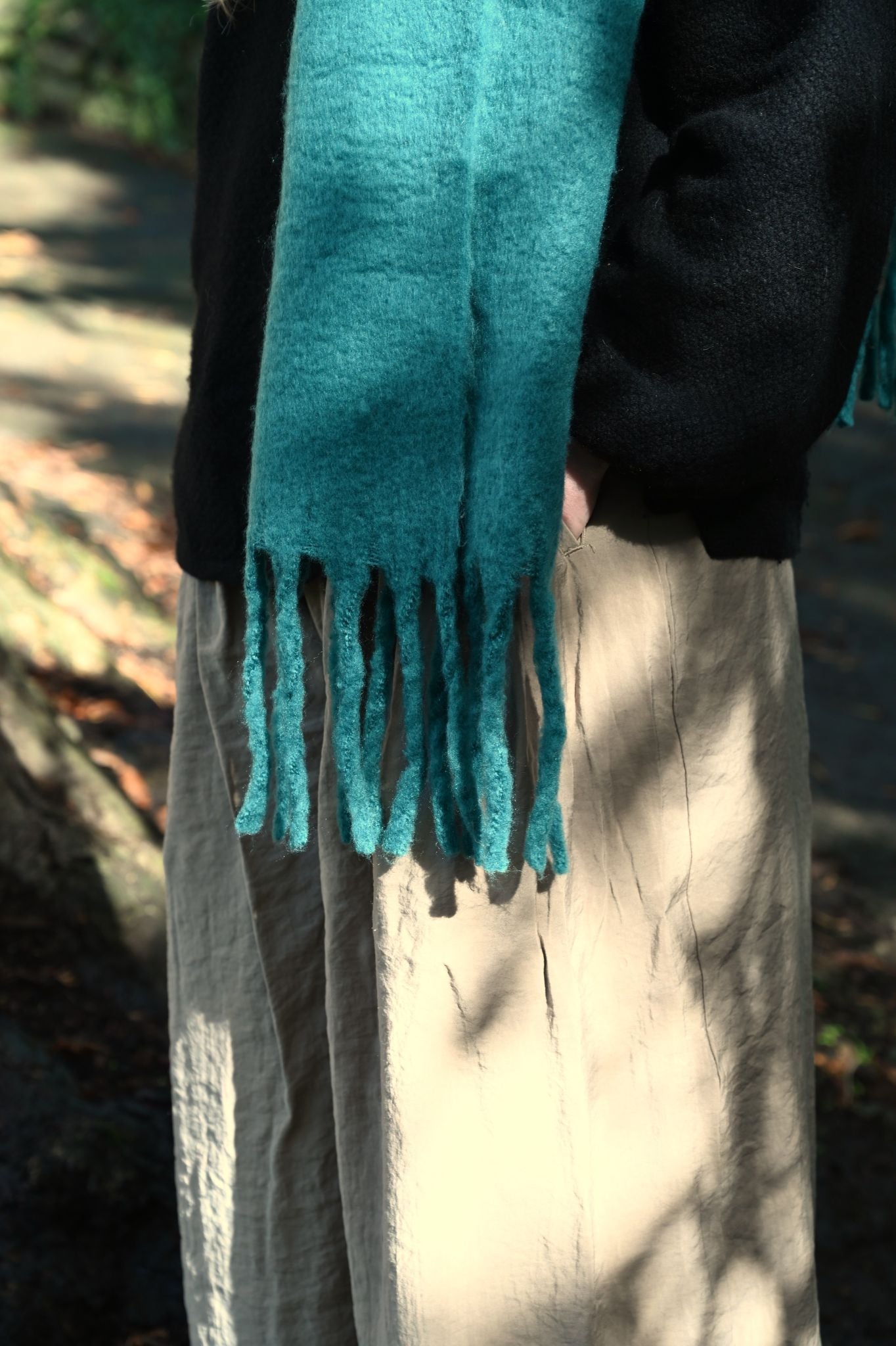 Person wearing a teal scarf with fringes in an outdoor setting