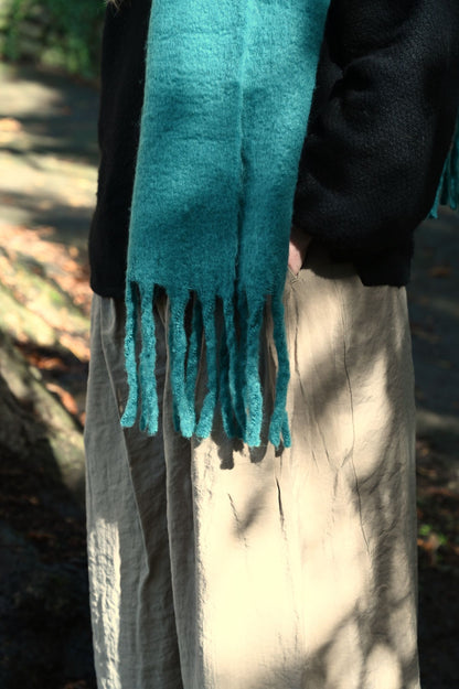 Person wearing a teal scarf with fringes in an outdoor setting
