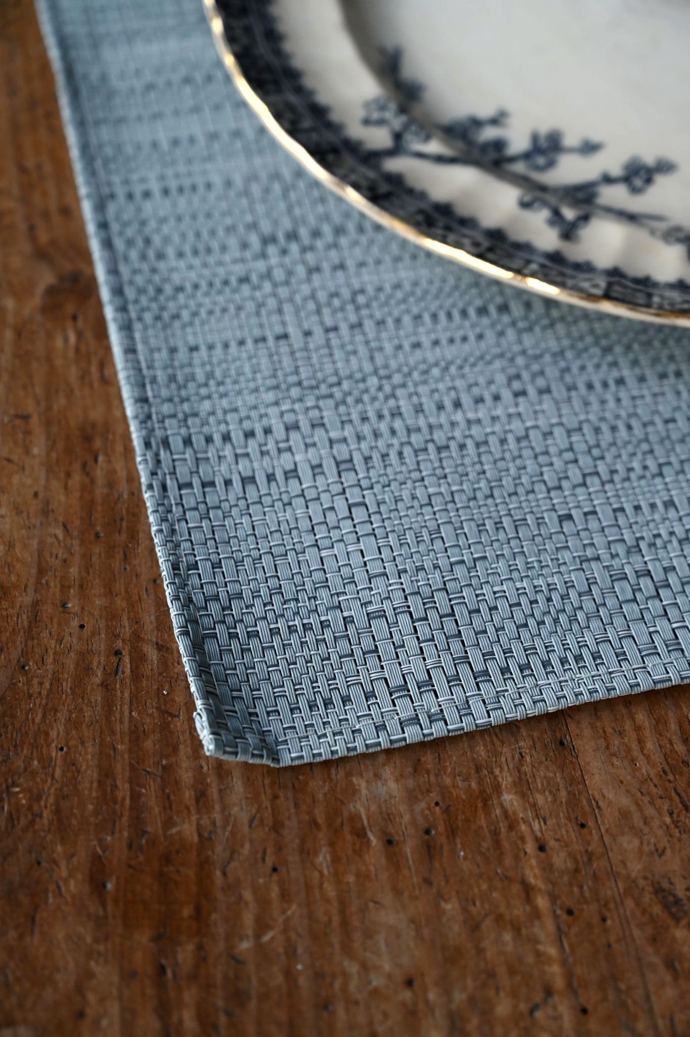 Textured blue placemat on a wooden surface with a white plate featuring blue patterns.