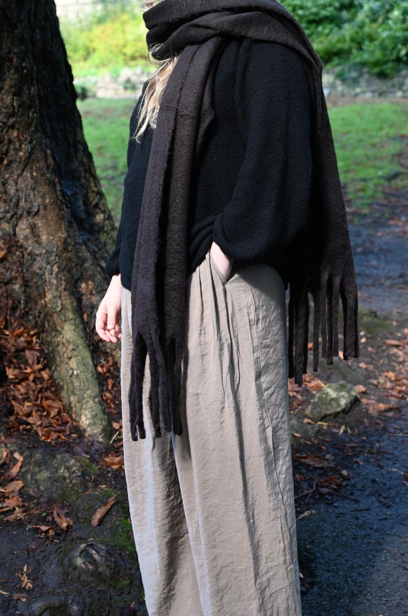 Person wearing a black sweater and beige pants with a dark brown scarf in an outdoor setting.