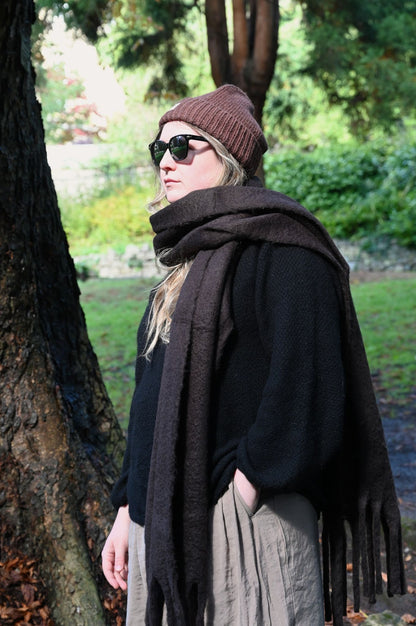 Person wearing a brown beanie and dark brown scarf in an outdoor setting