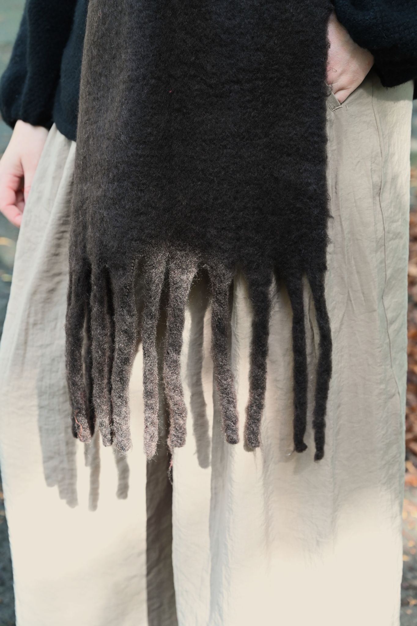 Dark brown fringed scarf draped over a person wearing light-colored pants.