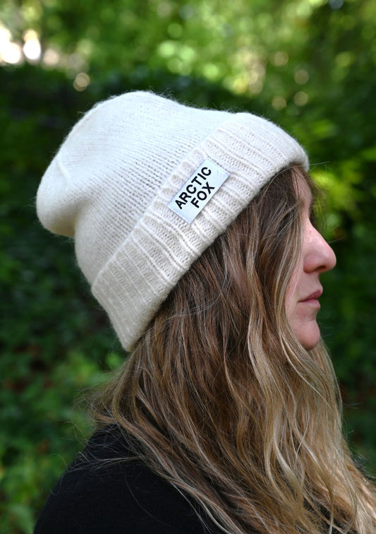Person wearing a white beanie with 'Arctic Fox' logo against a green background