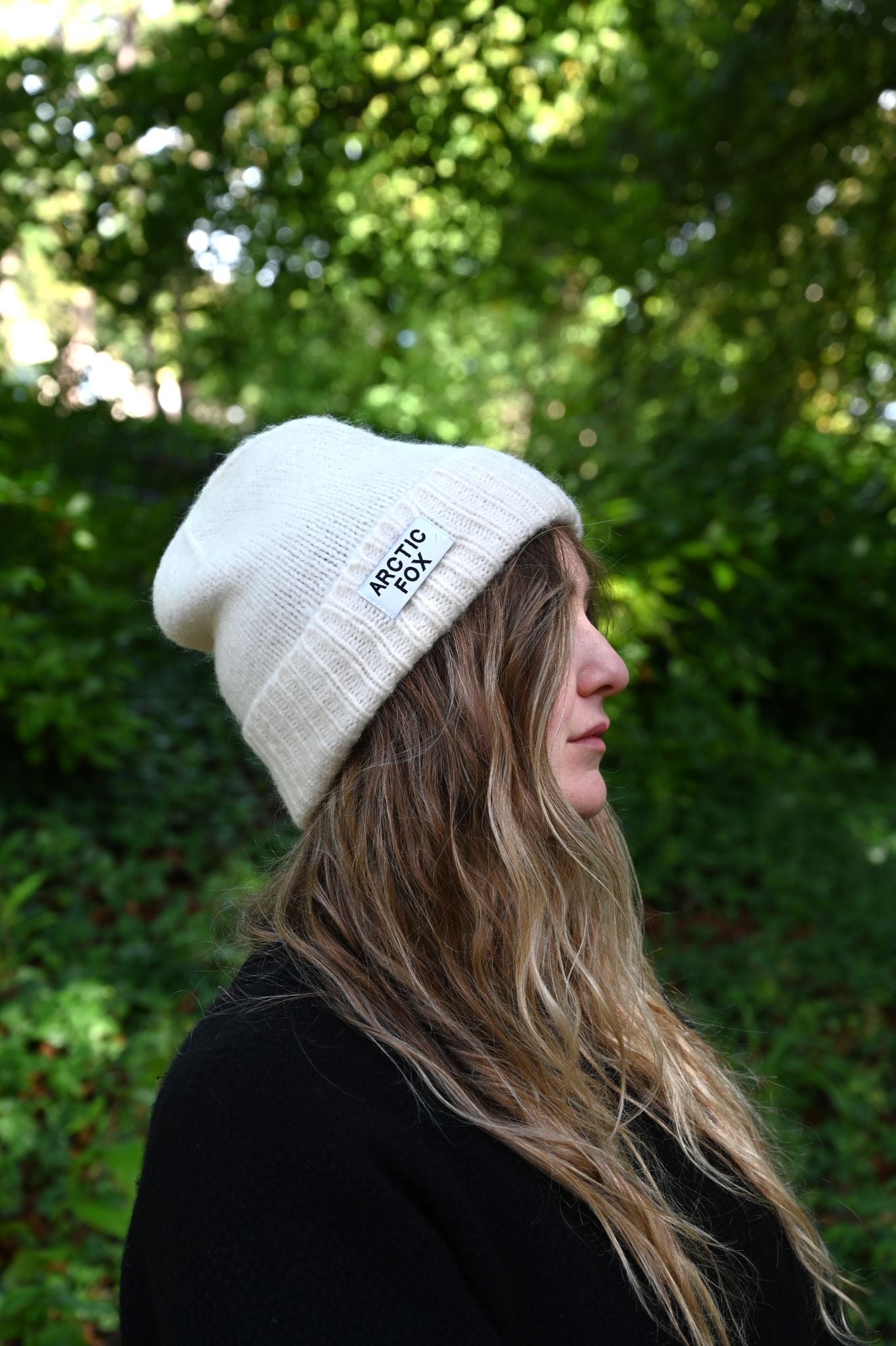 Person wearing a white beanie with 'Arctic Fox' logo against a green leafy background
