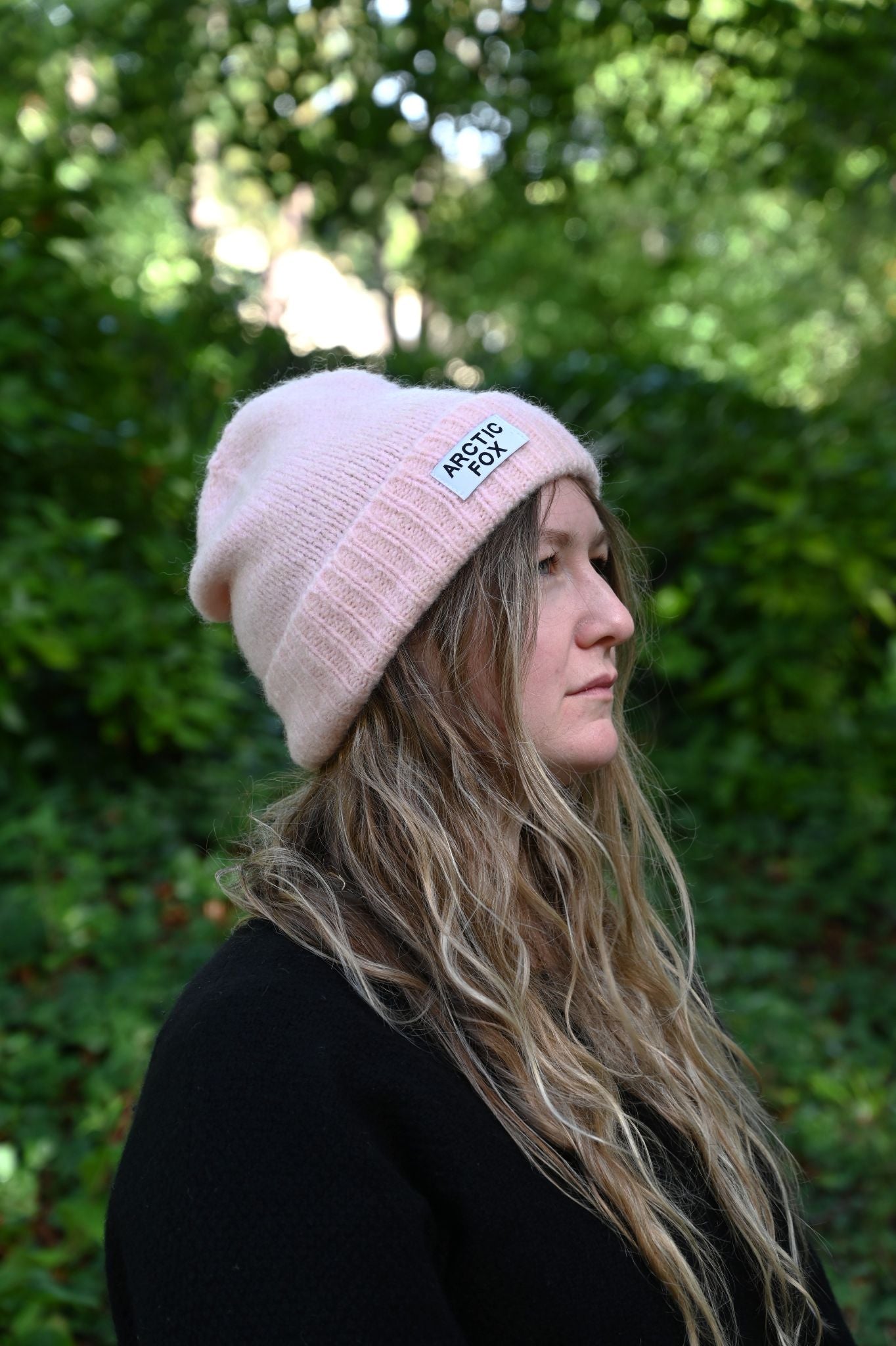 Person wearing a pink beanie with a logo outdoors