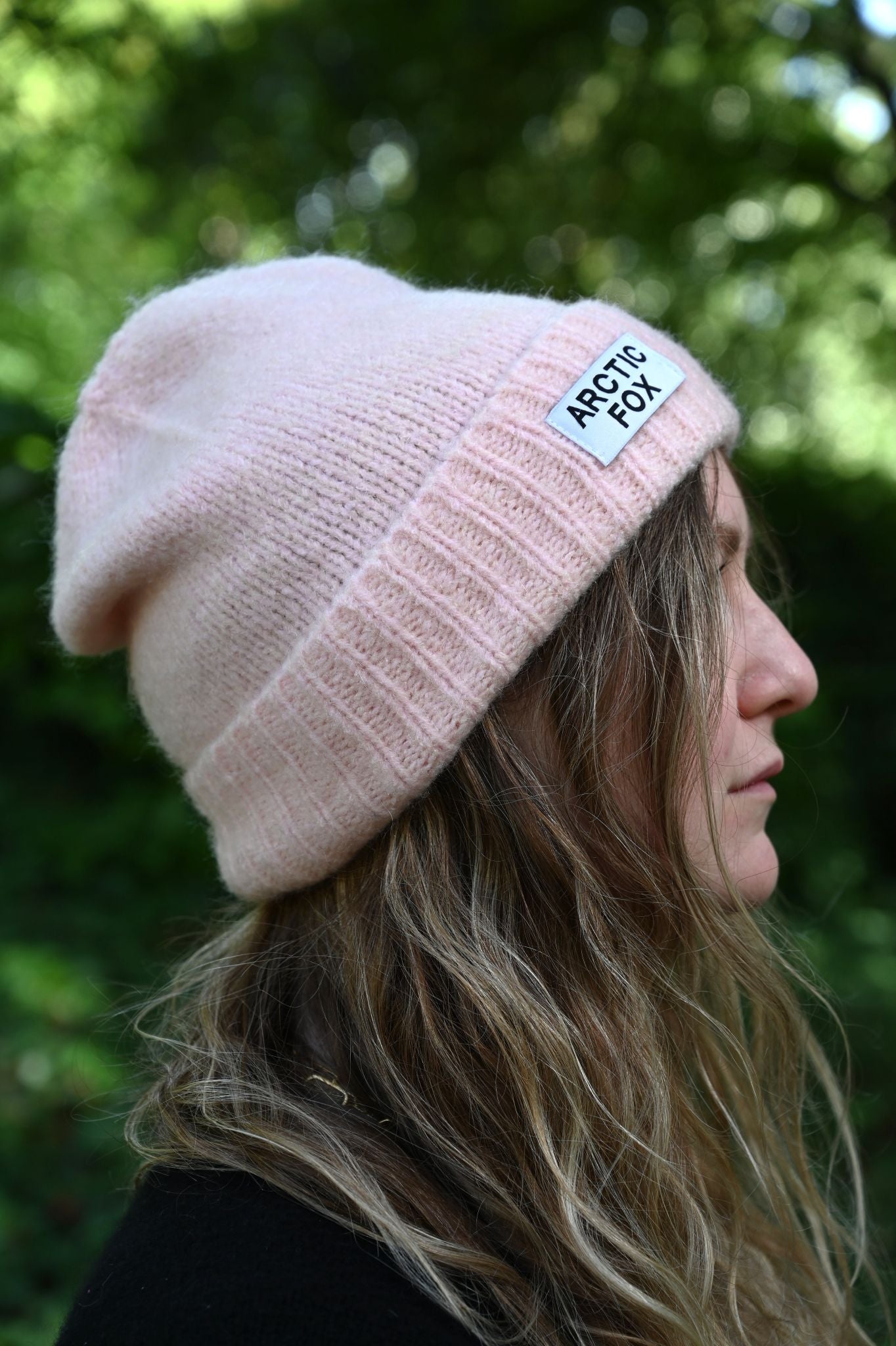 Person wearing a pink beanie with a brand logo against a blurred green background
