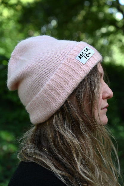 Person wearing a pink beanie with a brand logo against a blurred green background