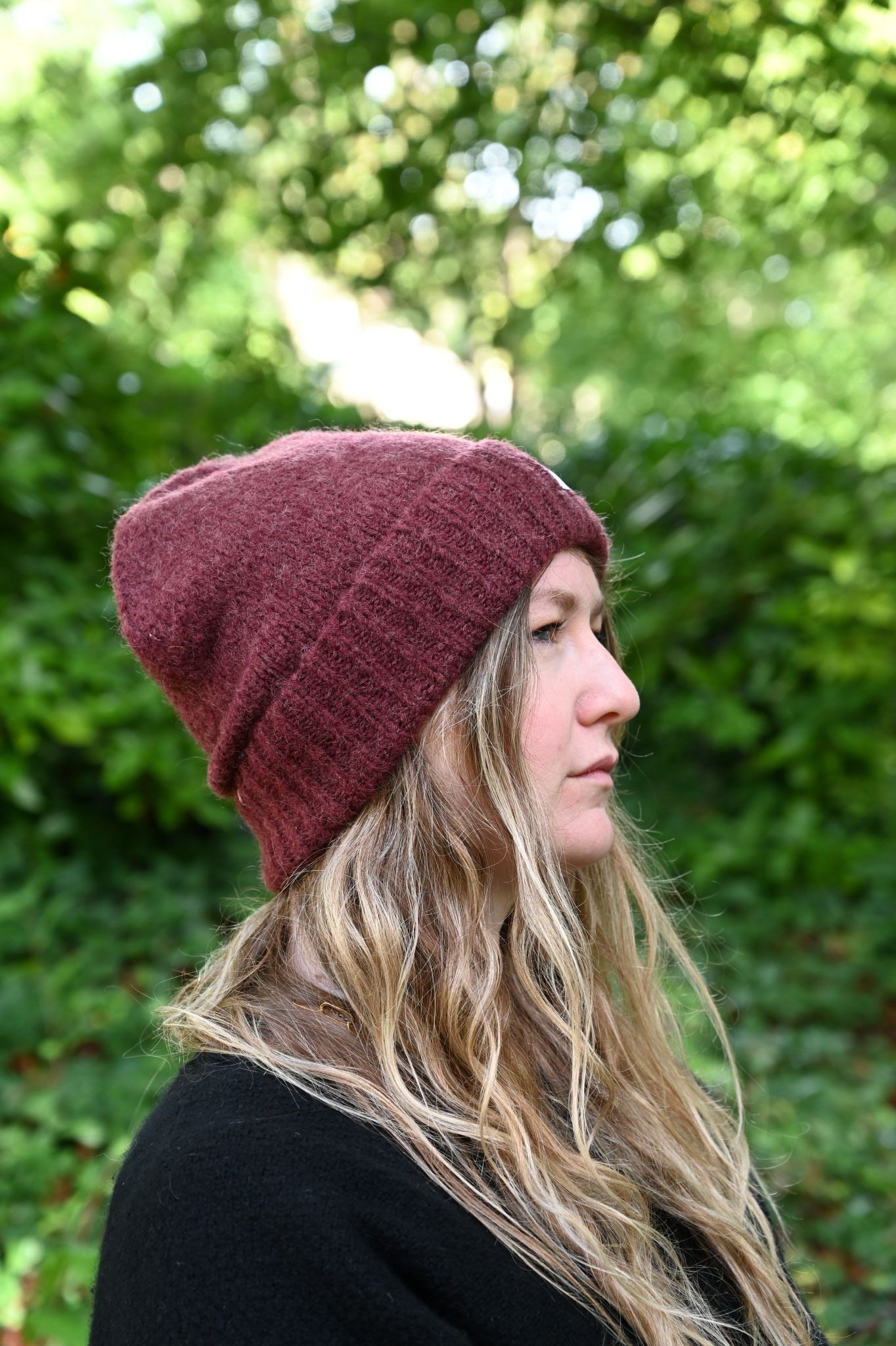 Person wearing a maroon beanie with blurred green foliage in the background
