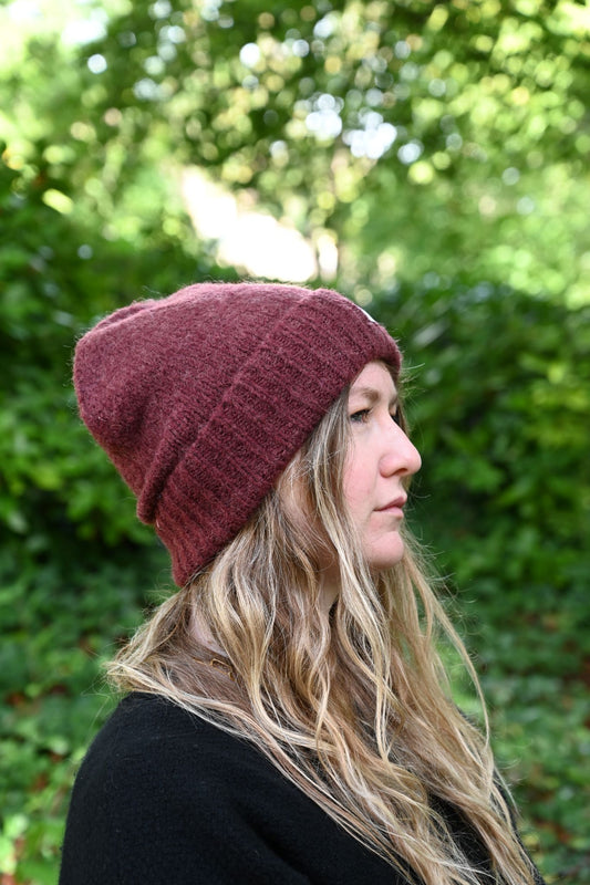 Person wearing a maroon beanie with blurred green foliage in the background