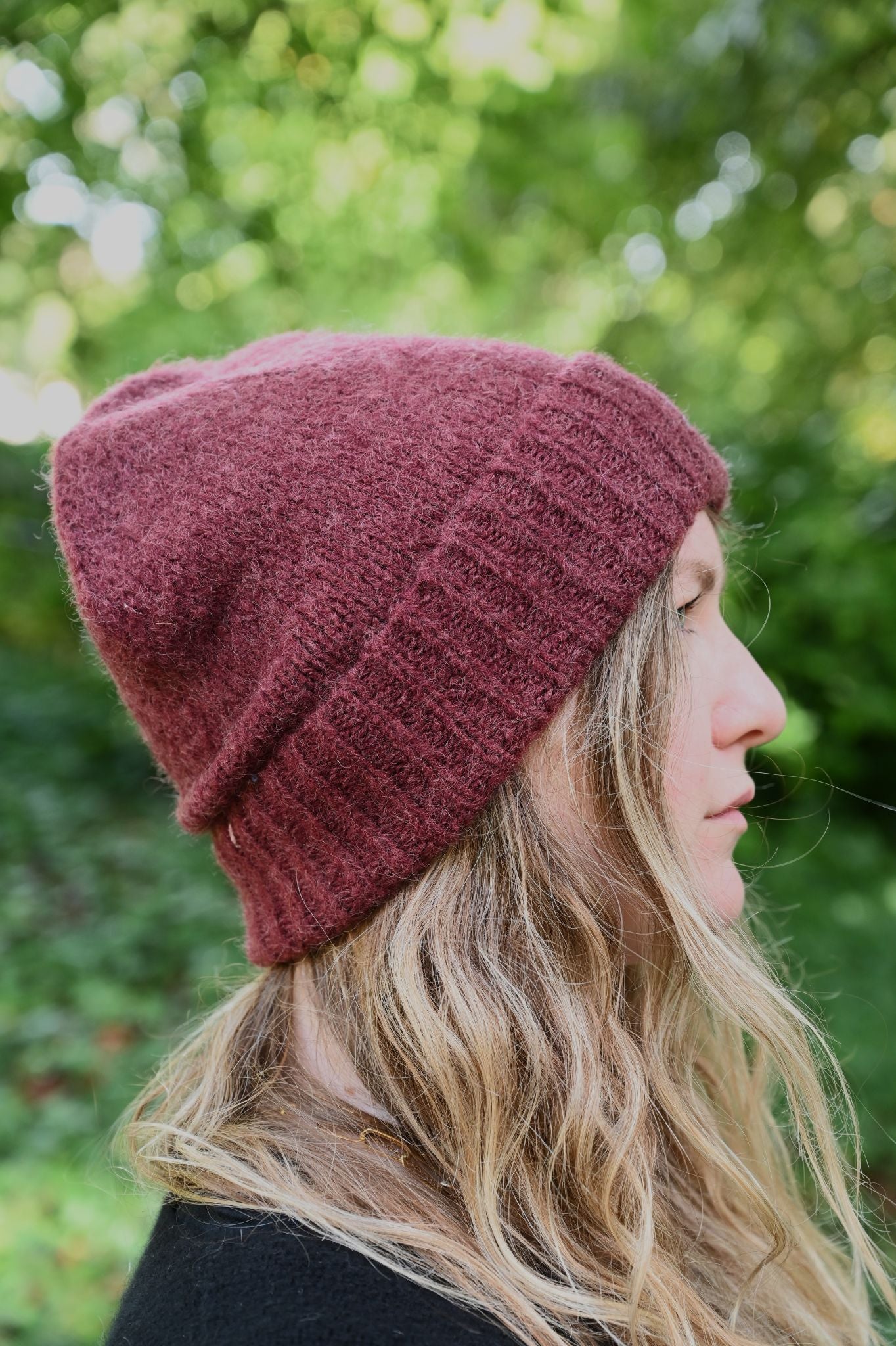 Person wearing a maroon knit beanie with a blurred green background
