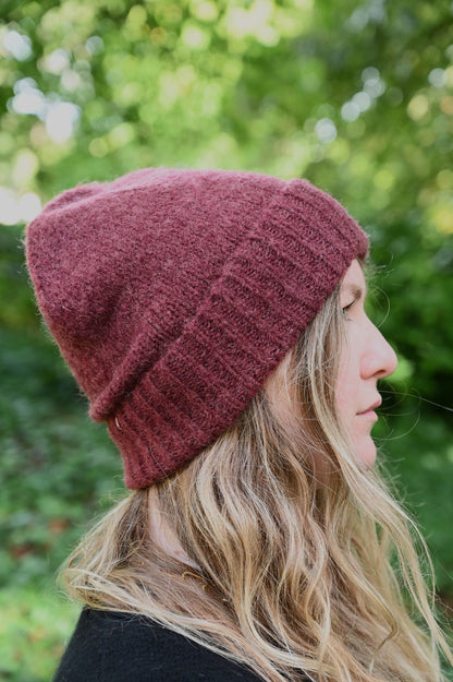 Person wearing a maroon knit beanie with a blurred green background