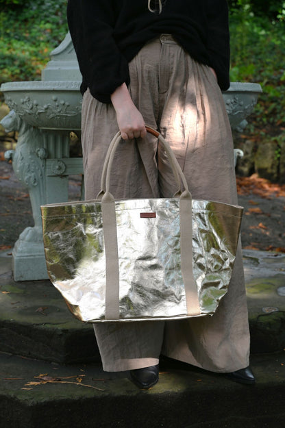 Person holding a reflective pale gold tote bag outdoors
