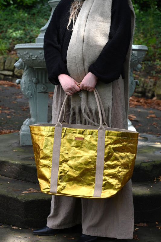 Person holding a gold tote bag in an outdoor setting